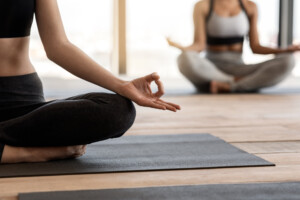 Zwei Frauen auf Yogamatten in Lotusposition in einem hellen Raum, die endlich mit Meditation anfangen 