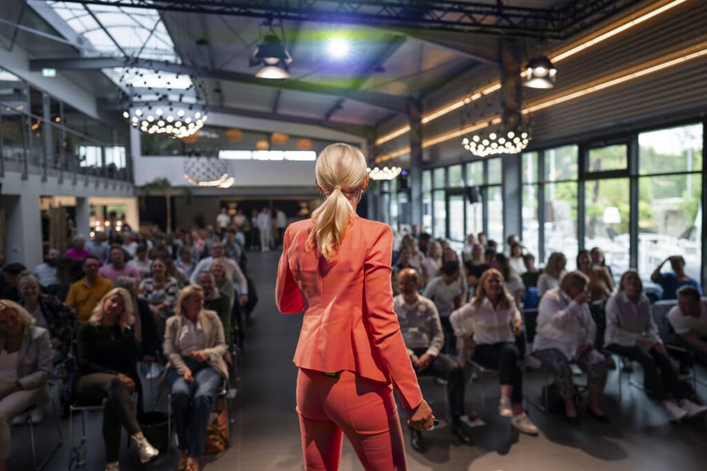 Kerstin Hardt steht bei Greator in einem orangefarbenen Outfit vor einer Menschenmenge